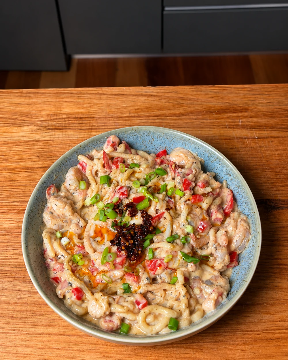 Bowl of udon in a creamy sauce with prawns, capsicum and chilli crisp
