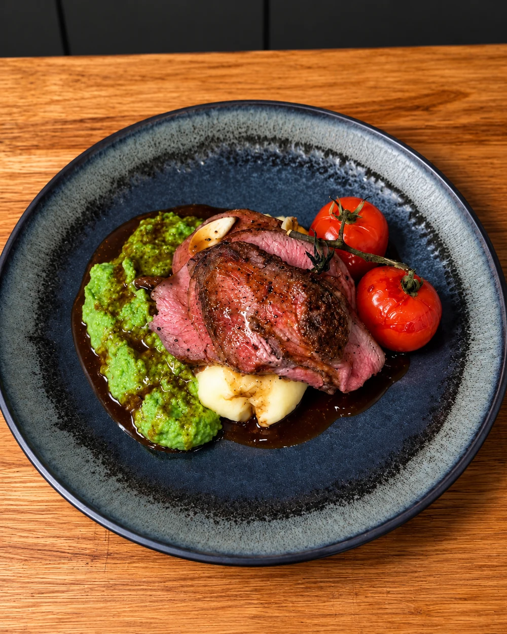 Sliced pink lamb leg with pea puree, mash and roasted vine tomatoes
